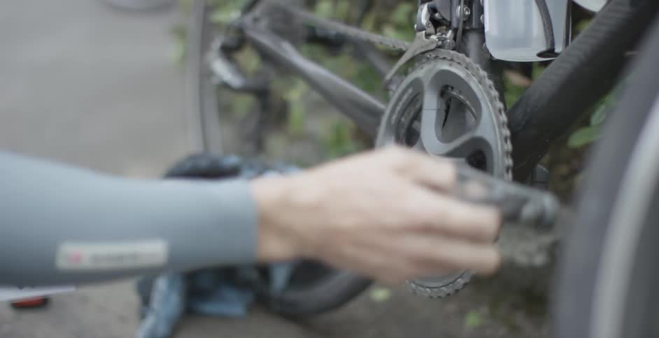 A bicyclist rotates his bike pedal with his hand and cleans the chain with a cloth