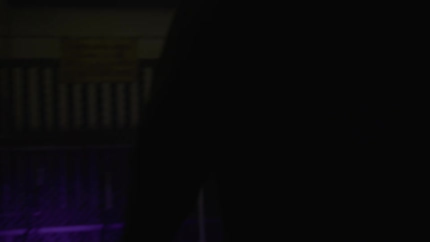 Men open a gate inside a dark building and approach lacrosse equipment