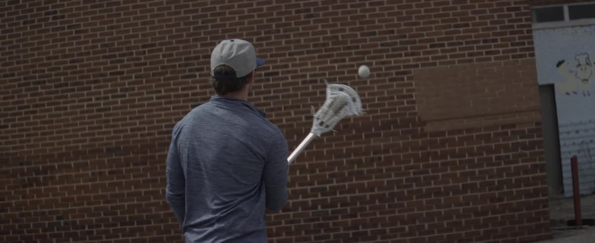 A man is tossing a ball at a wall with a lacrosse stick