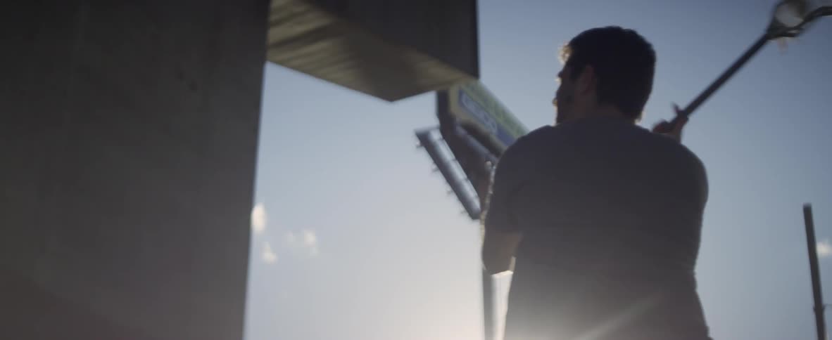 A man bounces a ball off a building and catches it with a lacrosse stick