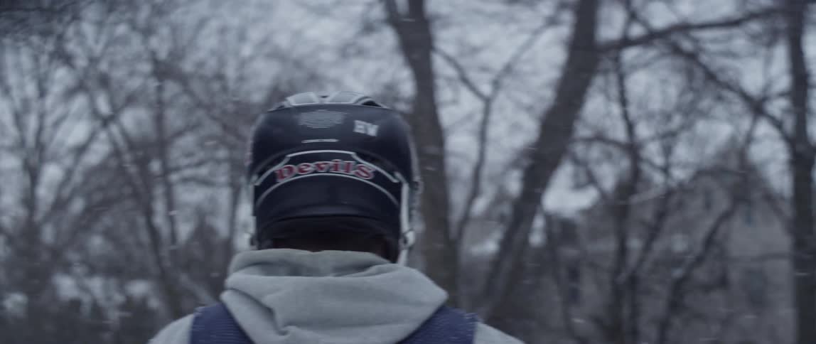A man in a sports helmet walks outside while it snows
