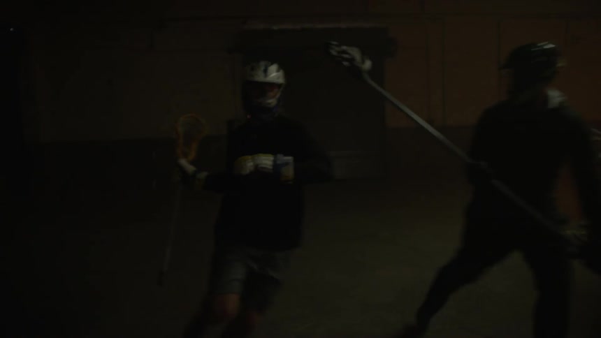 A group of men play lacrosse in a dimly lit arena