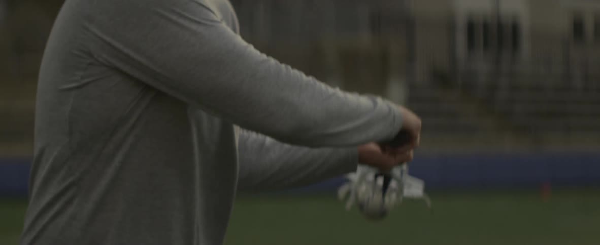 Man picks up a ball with a lacrosse stick and throws the ball