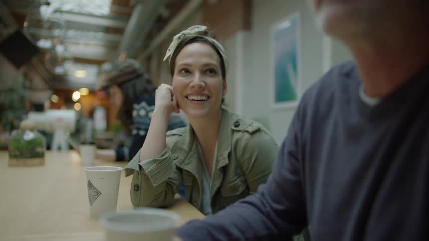 A woman sitting at a cafe counter smiles at the man beside her