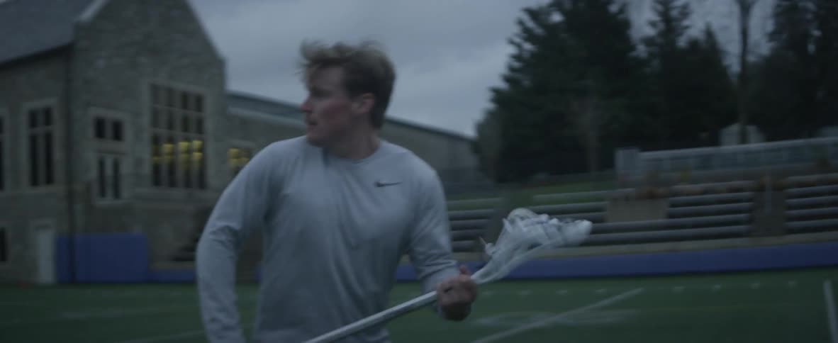 A man plays lacrosse alone on a sports field