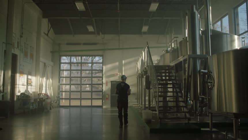 A person walks through a distillery with a clipboard