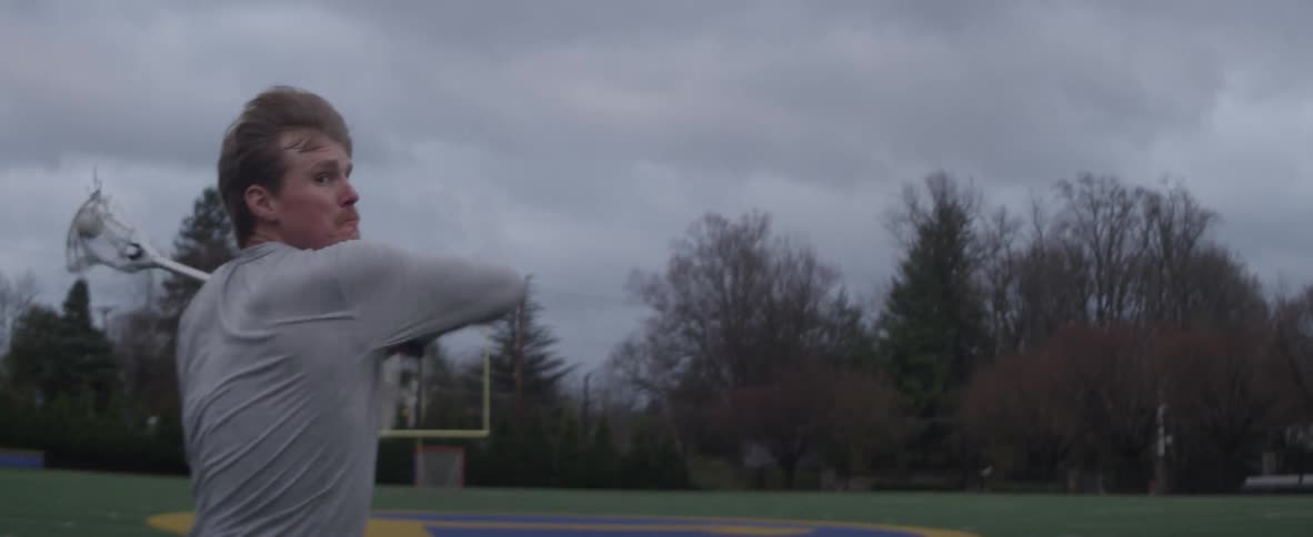 Man practices lacrosse outside in a field on a cloudy day