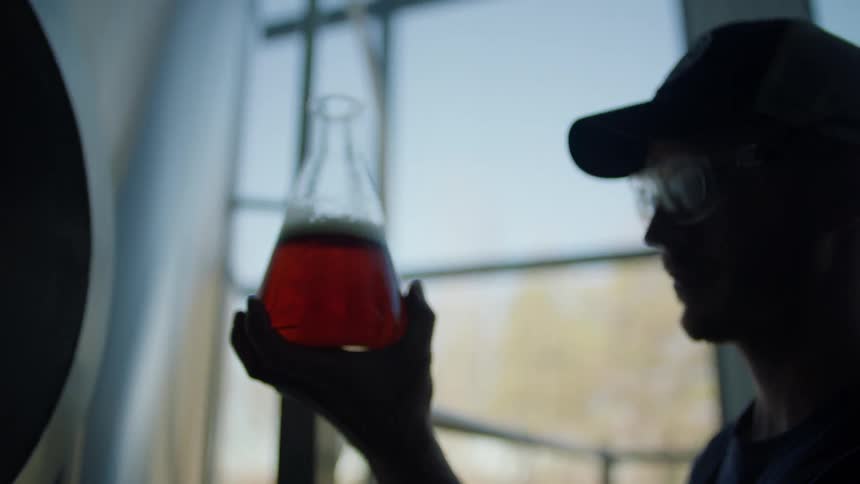 Man wearing safety glasses fills a beaker with liquid