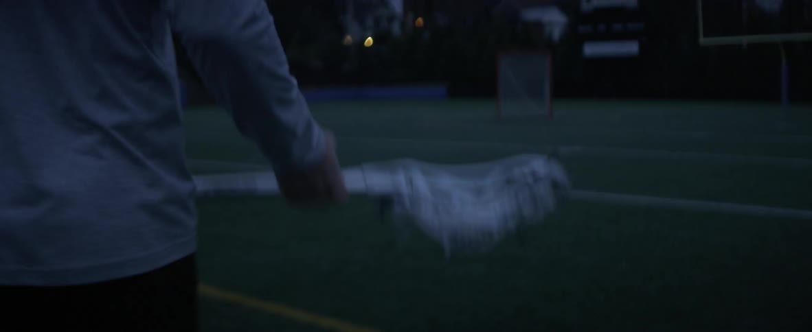 A man holding a lacrosse stick walks across a field