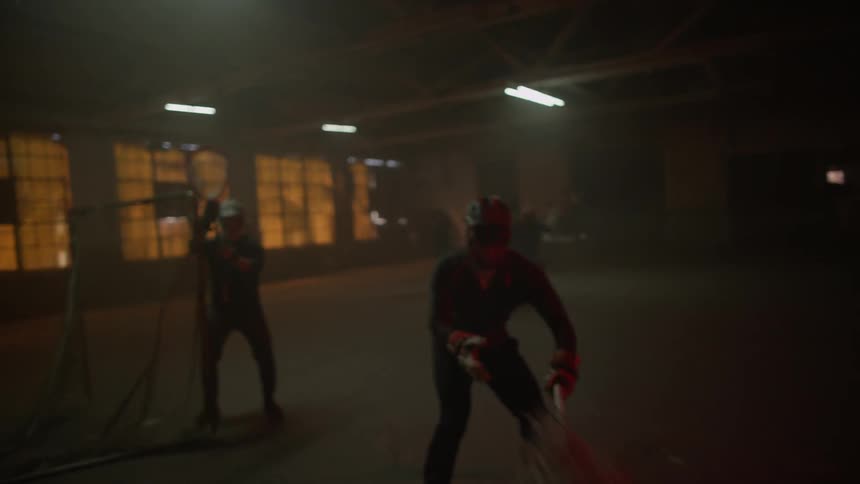 Several people play lacrosse in a dark warehouse