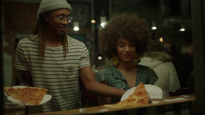 Man puts a large piece of pizza in front of a woman and sits down with his own slice