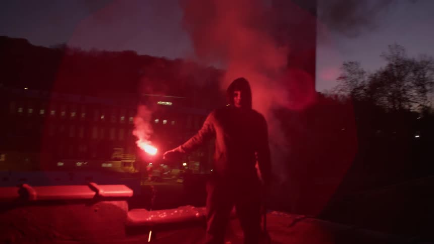 Man outside at night on building roof holding flare in hand