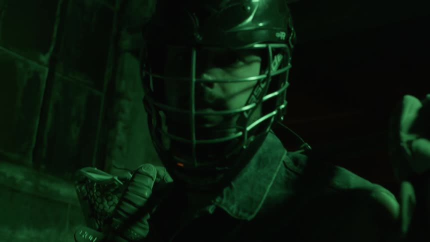 A man in lacrosse gear turns around in a dimly lit room