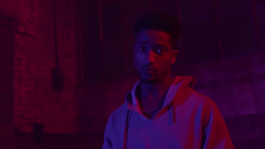 A man in a hoodie stands in a dimly lit room