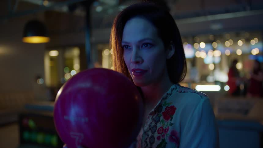 A woman holding a bowling ball points to people behind her
