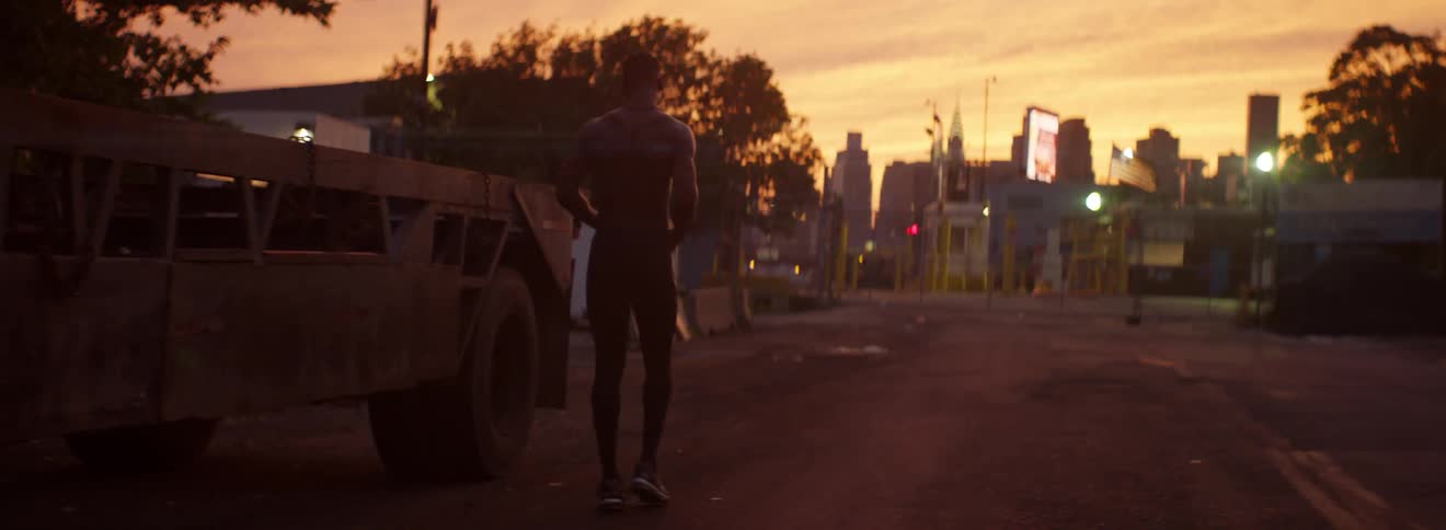 A male athlete walks down the middle of the street at dusk