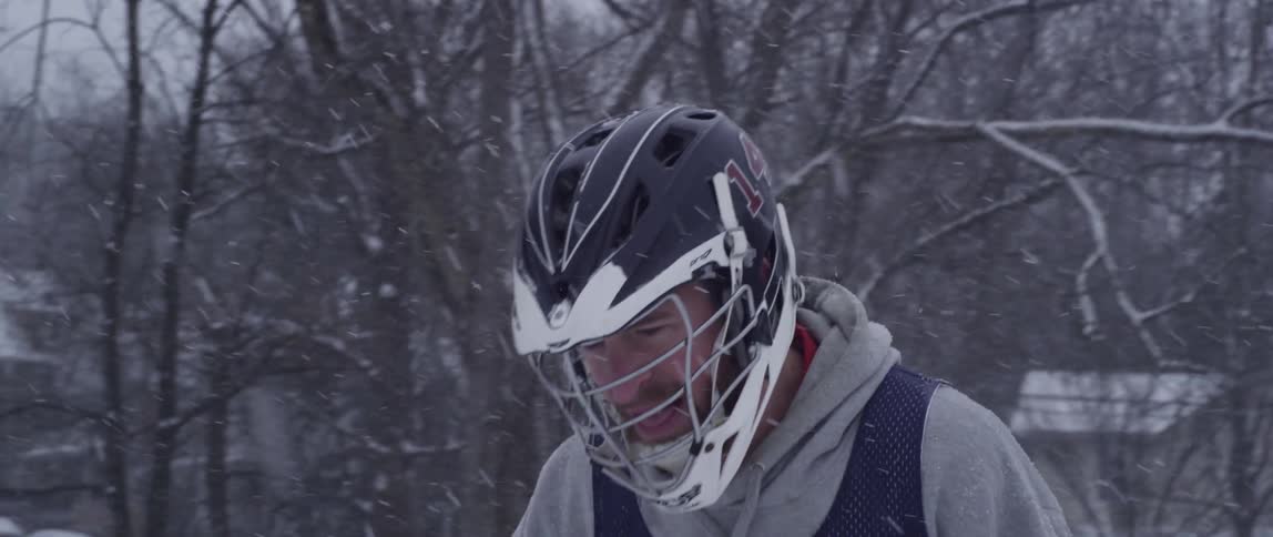 A man is walking with a lacrosse stick as it snows