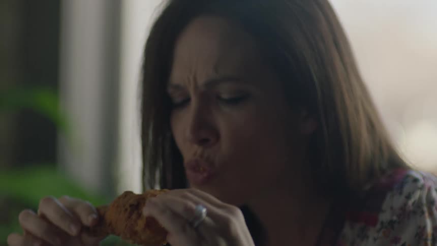 A woman eats a piece of fried chicken