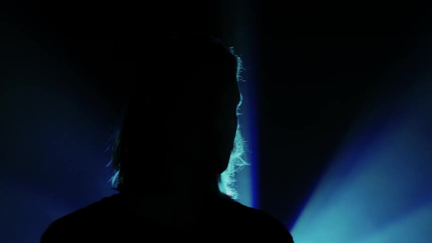 Man standing in the dark while blue colored lights flash behind him