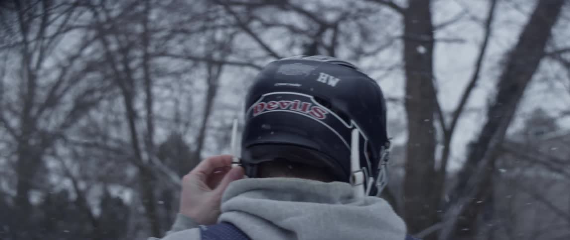 A man in a sports helmet walks outside while it snows