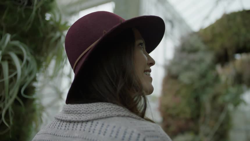 A woman smiles and looks around as she stands in a greenhouse