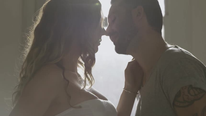 Man and woman stand close to each other next to a window on a sunny day