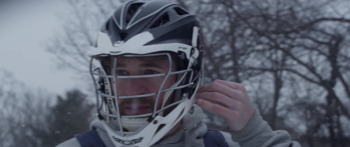 A man in a sports helmet walks outside while it snows