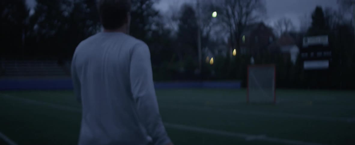 A lacrosse player holding a stick is walking on a field
