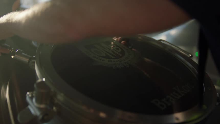 A man lifts the lid on a vat in a brewery