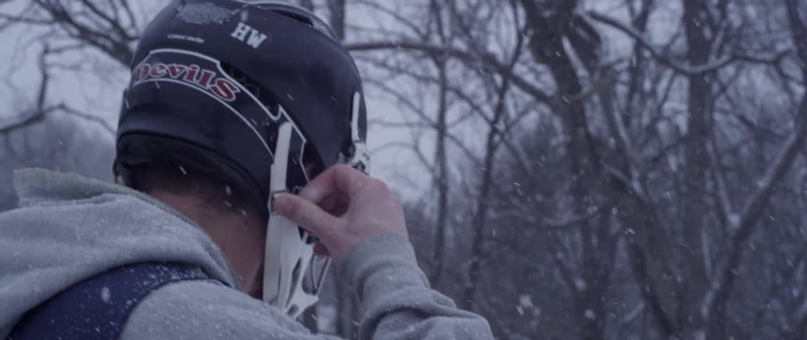 A man walks in the snow wearing a lacrosse helmet