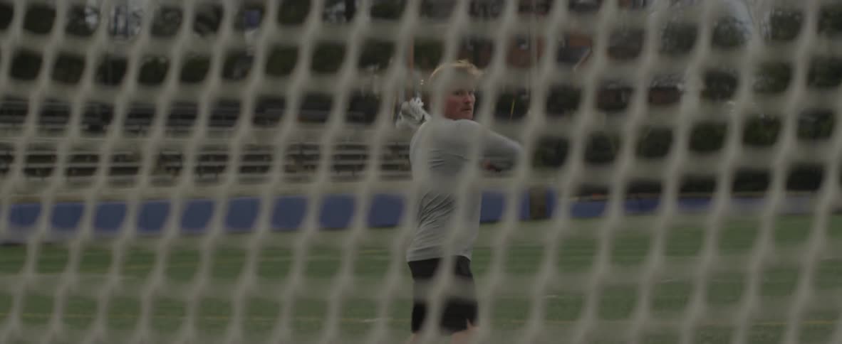 Man uses lacrosse stick to throw a ball into a goal net