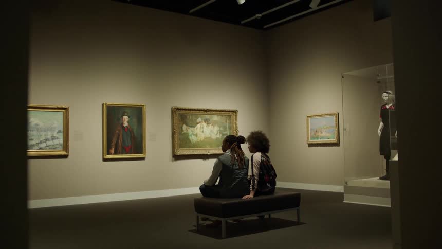 Two people sit down and view art in a gallery