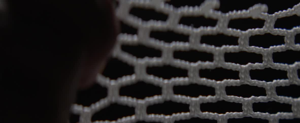 Hands pull at a webbed fabric and expand it
