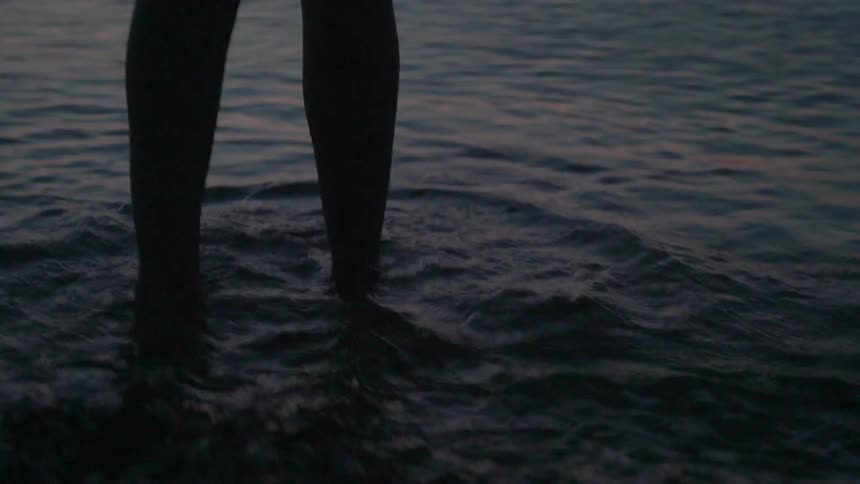 A woman steps into the ocean at sunset