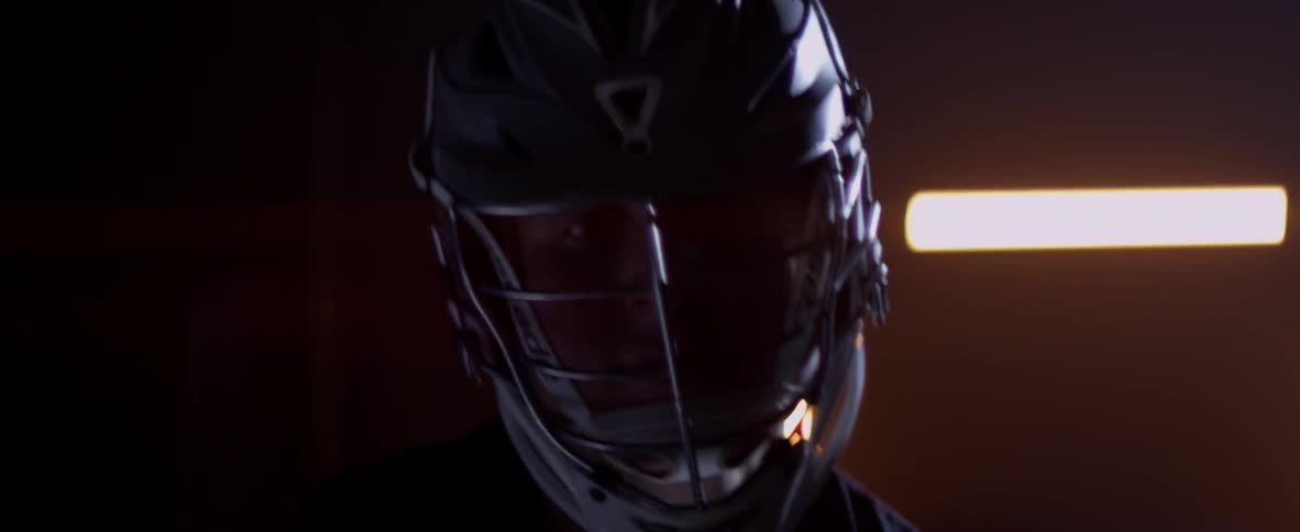 A man wearing a lacrosse helmet twirls a stick