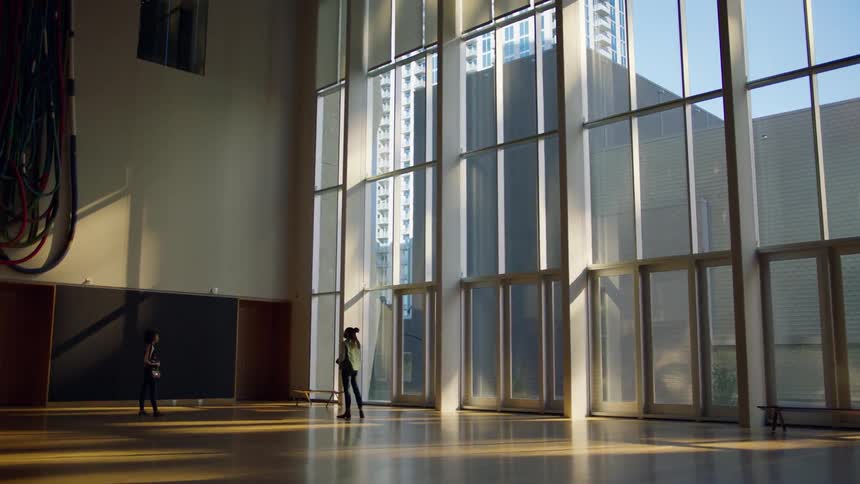 Two people stand in a large open room with tall windows
