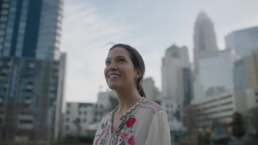 A woman smiles and looks around at buildings in the city