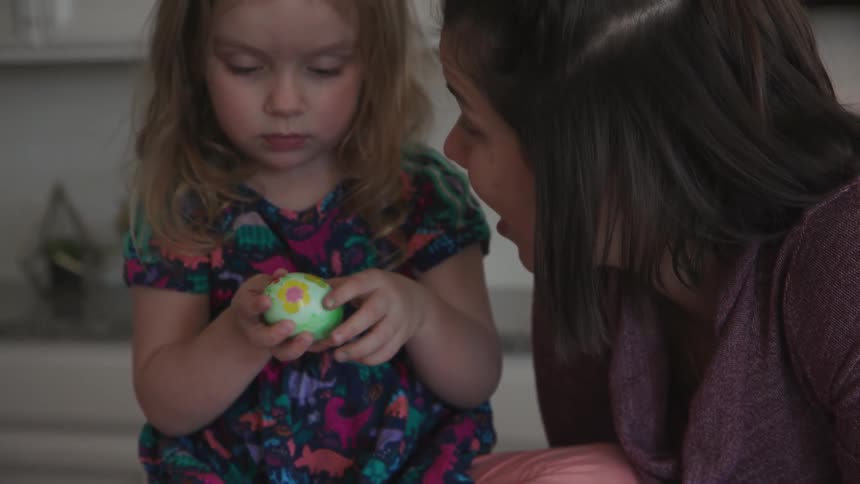 Woman talks to a child who is decorating an easter egg
