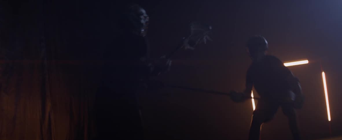 Two men play lacrosse in a dimly lit arena