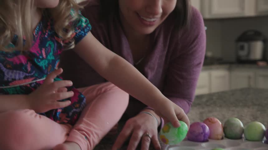 A woman smiles and laughs with a young girl who dyed eggs