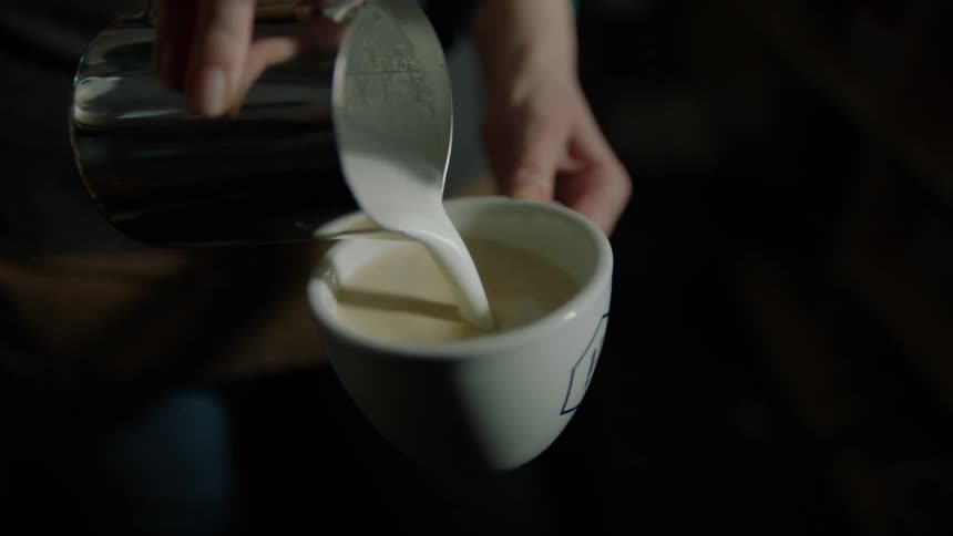 A person is swirling cream into a coffee cup