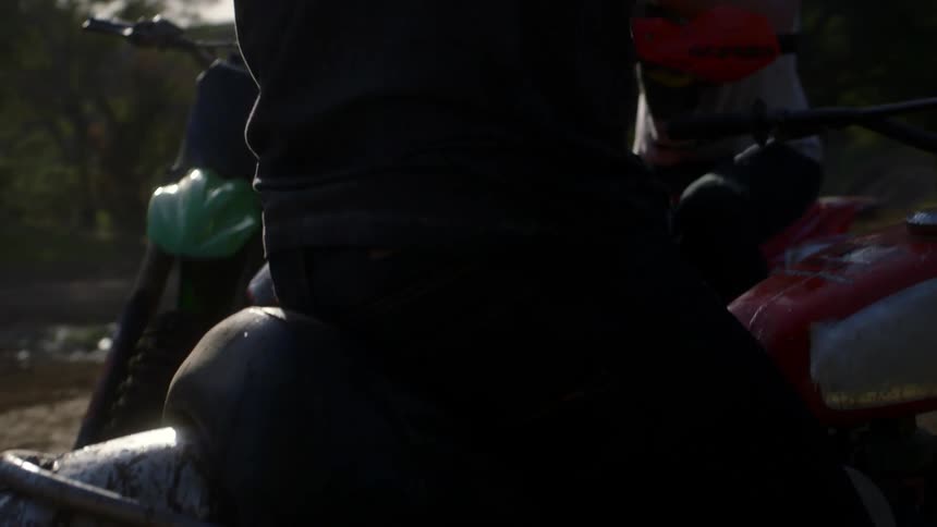 People on dirt bikes talk while stopped on a muddy trail