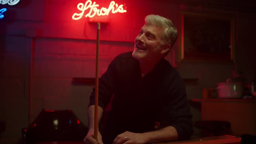 A man smiles while playing pool with another person