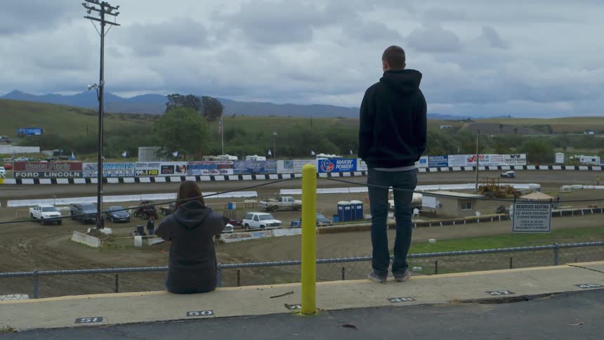 A man and woman watch cars racing on a track below
