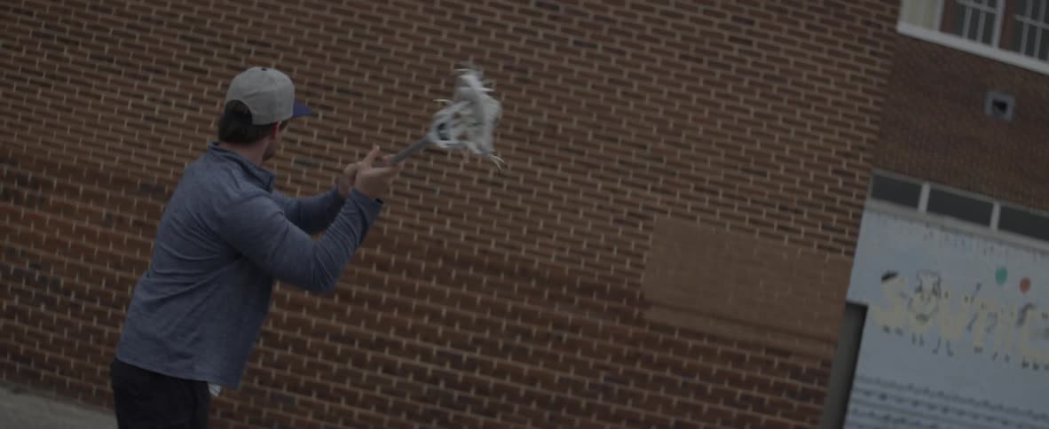 A man is tossing a ball at a wall with a lacrosse stick