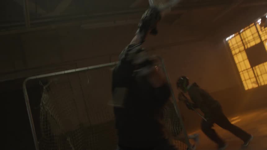Several people play lacrosse in a dark warehouse