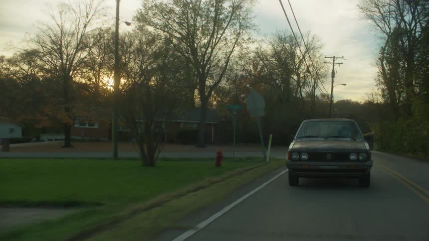 Old car driving down neighborhood street as sun sets