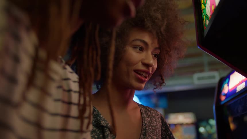 A woman and man talk as they play an arcade machine