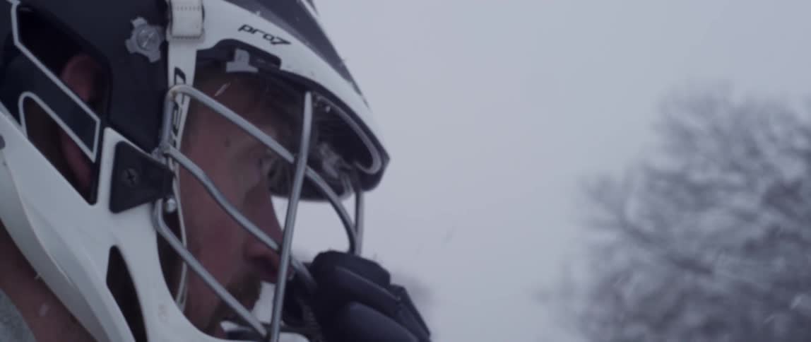 Snow falls on a man in a sweatshirt and sports helmet