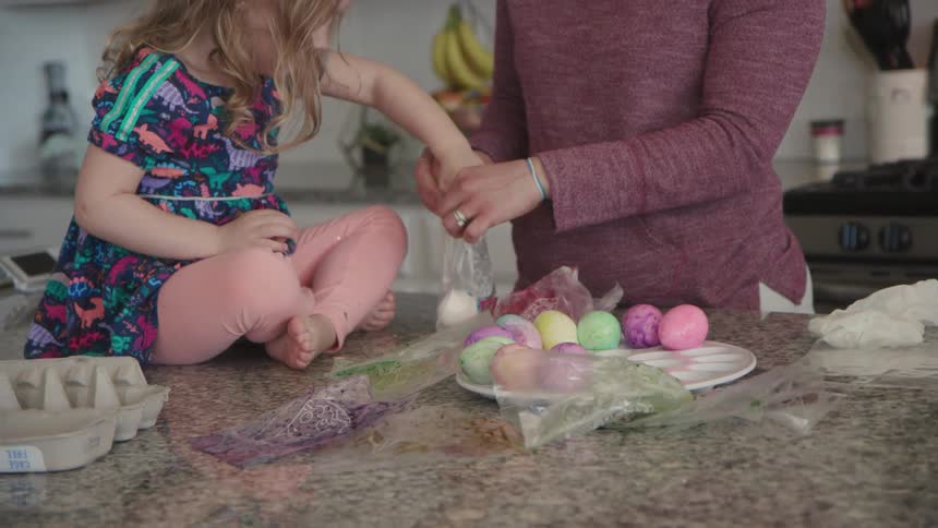 A mom and young girl decorate easter eggs in a kitchen